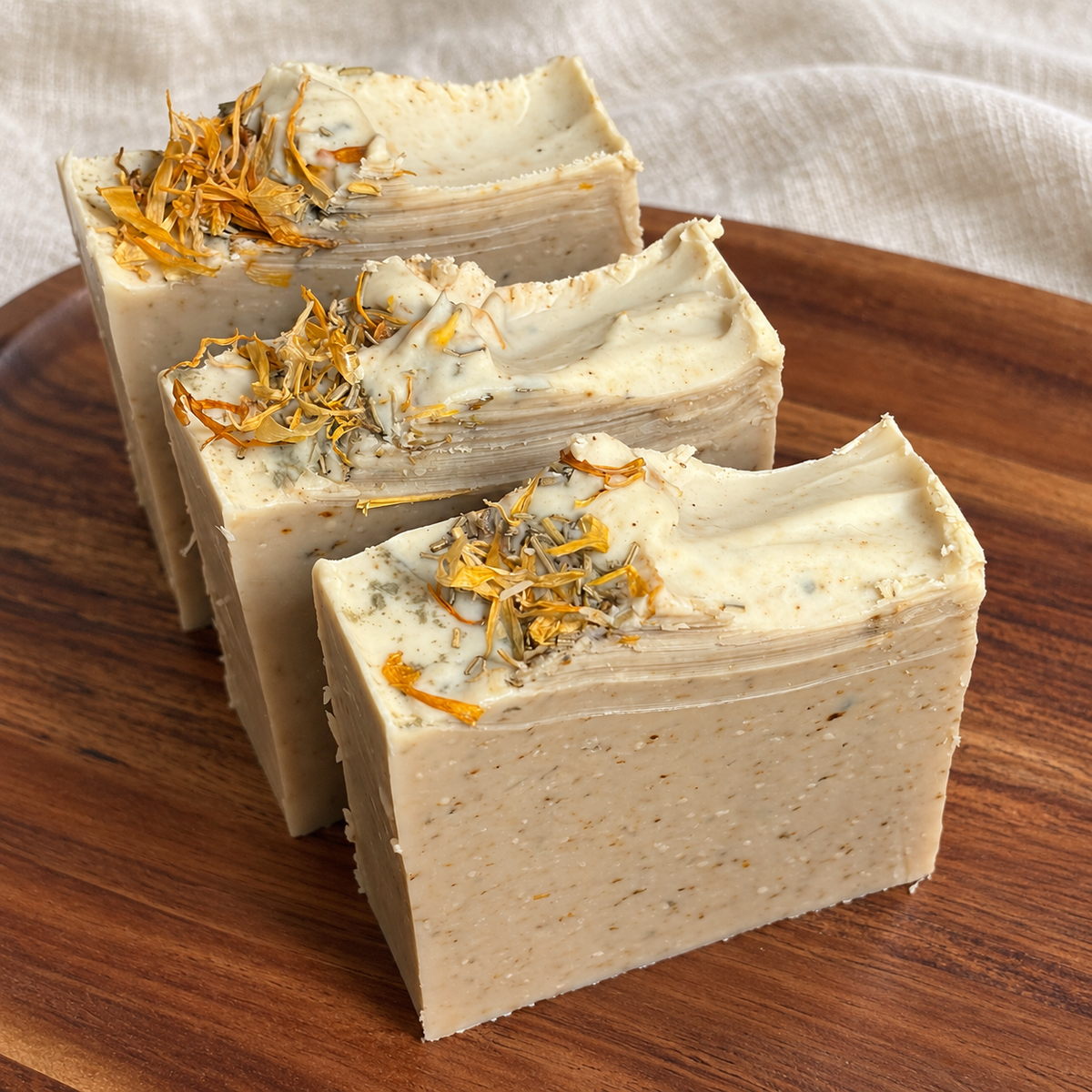 The Herbalist honey and beeswax soap bars with dried botanical tops on a wooden tray