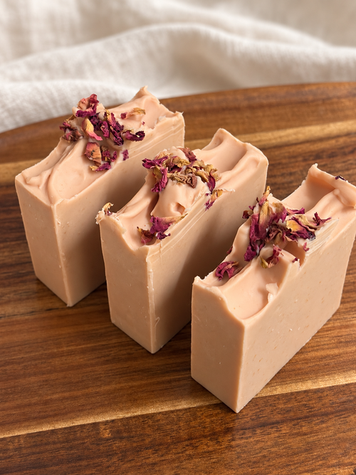 The Still Room honey and beeswax soap with blush pink sculpted tops and dried rose petals on a wooden tray