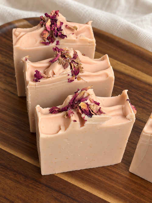 The Still Room honey and beeswax soap with blush pink sculpted tops and dried rose petals on a wooden tray