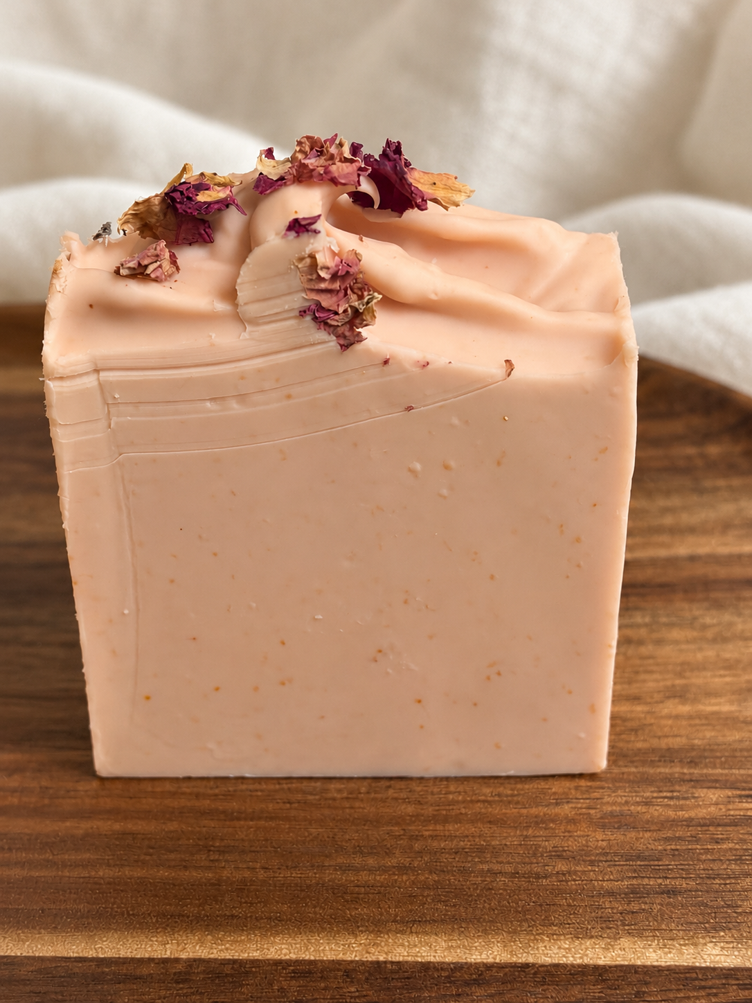 The Still Room honey and beeswax soap with blush pink sculpted tops and dried rose petals on a wooden tray